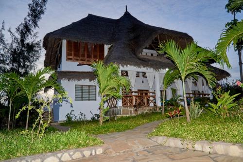 a white house with a thatched roof and palm trees at Beach Way Villa in Malindi
