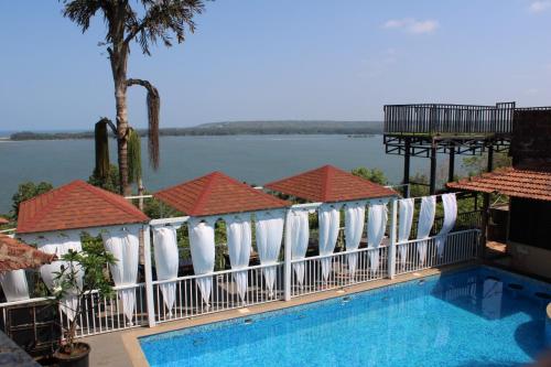 a swimming pool with white chairs and a view of the water at Raposo Resorts in Vagator