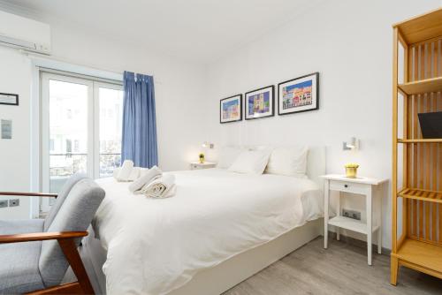 ein weißes Schlafzimmer mit einem großen Bett und einem Stuhl in der Unterkunft AL d' Cacilhas Studio in Almada