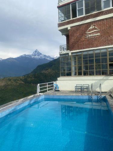 a hotel swimming pool with mountains in the background at Dhikidada Resort in Pokhara