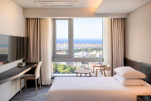 a hotel room with a bed and a desk and a large window at Gloucester Hotel Jeju in Jeju