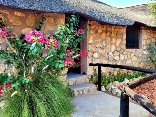 a stone house with pink flowers in front of it at Kapika Waterfall Lodge in Epupa