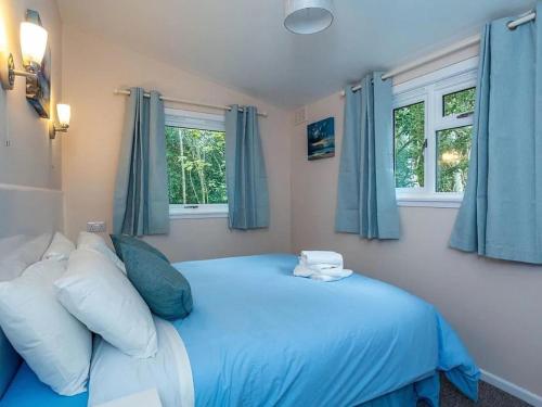 a bedroom with a blue bed and two windows at Bridgend Chalet on Reelig Estate Near Inverness in Kirkhill