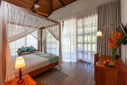 Anse Lazio Lodge في آنس لازيو: غرفة نوم مع سرير مظلة في غرفة مع نوافذ
