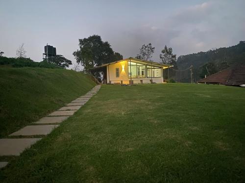 a small house on a grassy field with a building at Thendral: Delightful homestay on a hill near Ooty in Naduvattam