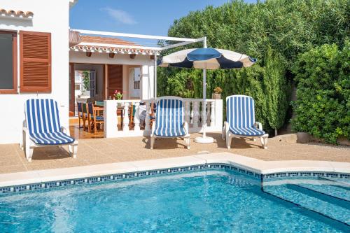 two chairs and an umbrella next to a swimming pool at Villa JOJO & CLEO in Port d'Addaia