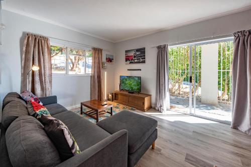 a living room with a couch and a tv at Die Brandhuis Sleeps 4, One minute walk to the Beach! in Gordonʼs Bay
