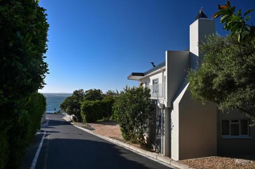 a white house on a road next to the ocean at Die Badhuis, for Fabulous living! Sleeps 4, Private pool in Gordonʼs Bay