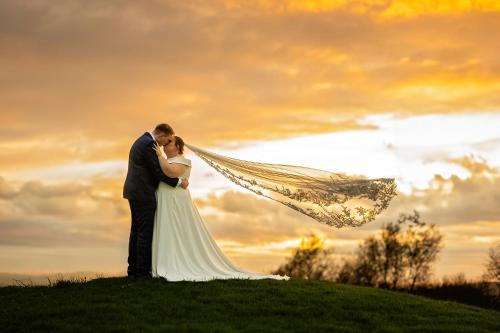 a bride and groom standing on a hill with their veil at Mendip Spring Golf and Country Club in Churchill