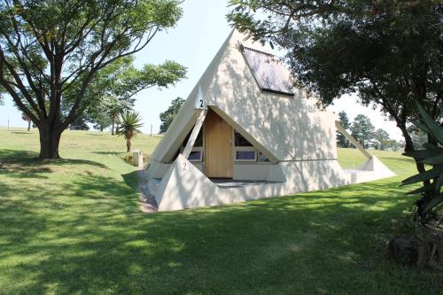 a house with a triangular roof on a grass field at Pyramids Motel in Van Reenen