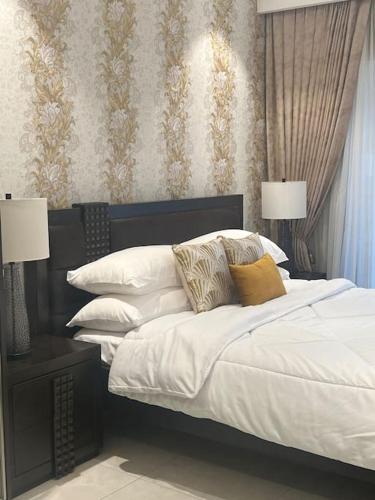 um quarto com uma cama com lençóis brancos e almofadas em Mirage Residence Apartment Accra em Acra