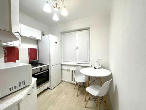 eine weiße Küche mit einem kleinen Tisch und Stühlen in der Unterkunft Квартира в самом центре in Qaraghandy