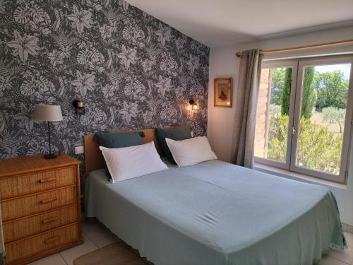 Schlafzimmer mit einem Bett mit blauer Bettdecke und einem Fenster in der Unterkunft Gîte Les Rapières in Gordes