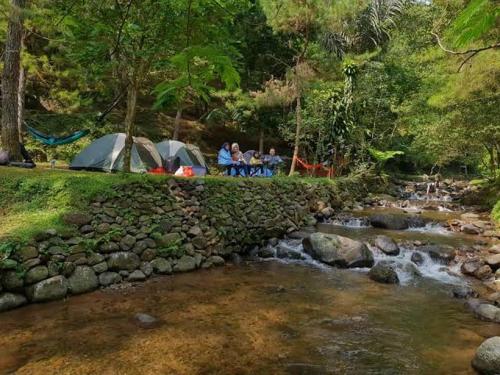 a group of people sitting next to a stream with tents at view cemping glamping in Bukittinggi