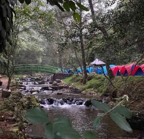 a stream with a group of tents and a bridge at view cemping glamping in Bukittinggi