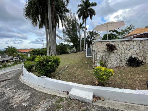 a retaining wall next to a house with an umbrella at Peaceful Palms Montego Bay in Montego Bay