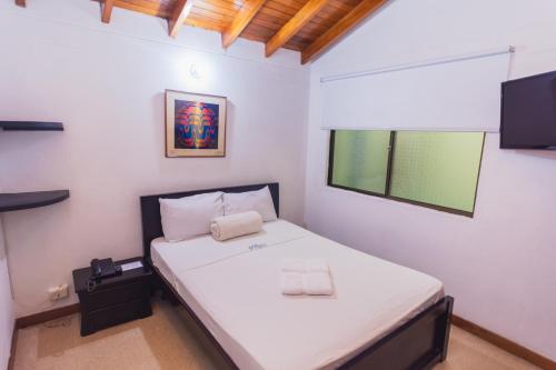 a bedroom with a bed with white sheets and a window at Hotel Guatatur in Guatapé