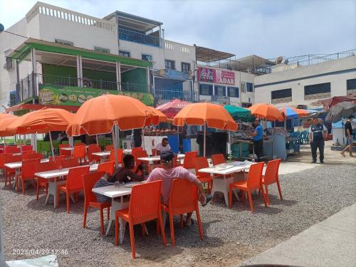 a group of people sitting at tables with orange umbrellas at Taghazout "luxe residence Tafoult" 3 pools and aquapark in Taghazout