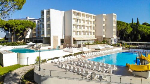a hotel with a pool and chairs and a building at Hotel Adria - All inclusive in Biograd na Moru