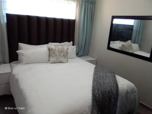 een slaapkamer met een wit bed en een spiegel bij Waterfall Ridge Apartments - Kick back and Relax in Midrand