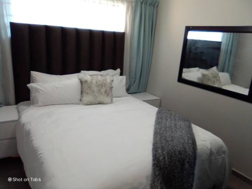 a bedroom with a white bed and a mirror at Waterfall Ridge Apartments - Kick back and Relax in Midrand
