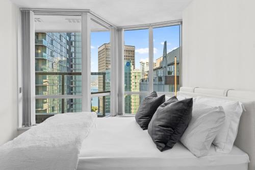 a white bed with black pillows in front of a window at Downtown Luxury 1BR Coal Harbour in Vancouver