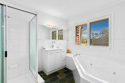 Baño blanco con bañera y lavamanos en WhiteSands Beachouse, en Urangan