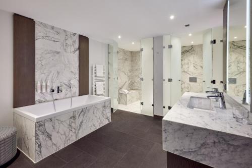 La salle de bains est pourvue d'une grande baignoire et de murs en marbre. dans l'établissement Le Méridien Frankfurt, à Francfort-sur-le-Main