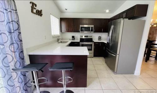 Una cocina con refrigerador y dos taburetes de bar. en Miramar Private Luxury Room/Bath/WiFi, en Miramar