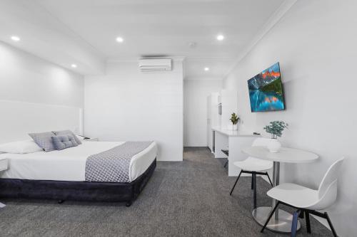 a white bedroom with a bed and a table and chairs at Shellharbour Village Motel in Shellharbour