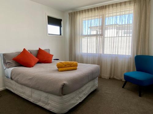 a bedroom with a bed with orange pillows and a blue chair at Style, Functional with Space in Twizel