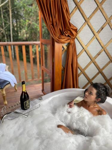 a woman laying in a bath tub with a bottle of wine at Glamping montain experience in São Joaquim