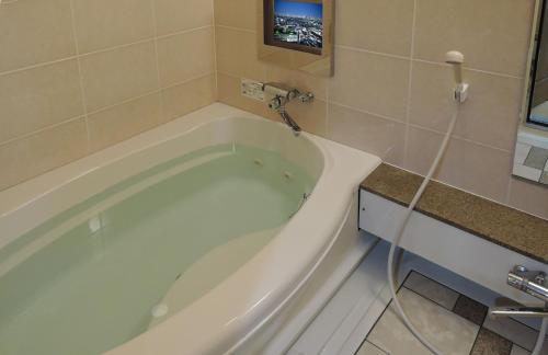 a bath tub in a bathroom with a tv on the wall at Hotel M in Oyodo
