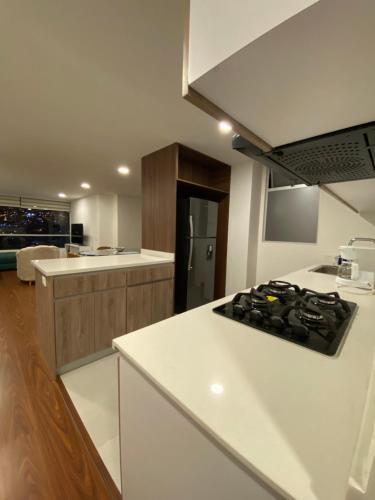 La cuisine est équipée de comptoirs blancs et de plaques de cuisson. dans l'établissement Apartamento panorámico de lujo en el Centro de Pasto, à Pasto