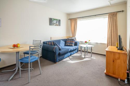 - un salon avec un canapé bleu et une table dans l'établissement Daffodil Motel, à Christchurch