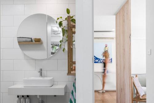 a bathroom with a sink and a mirror and a woman in the background at The Pool House - Byron Bay in Byron Bay