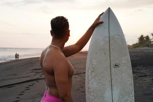 a man holding a surfboard on the beach at SHANTI SURF CAMP in El Paredón Buena Vista
