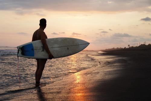 a man standing on the beach holding a surfboard at SHANTI SURF CAMP in El Paredón Buena Vista