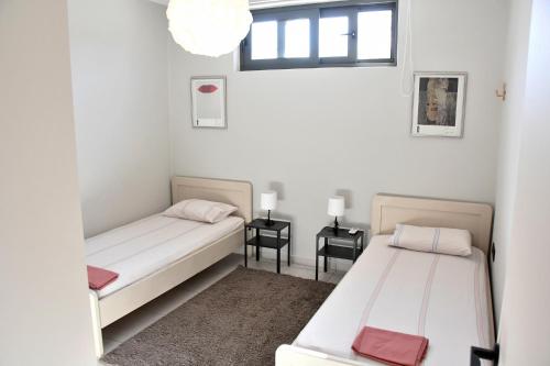 two beds in a room with two tables and a window at Polles Εlies Cozy Αpartment in Aegina Town