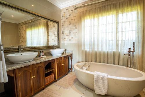 Andes Clarens Guesthouse في كلارينس: حمام به مغسلتين وحوض استحمام ومرآة