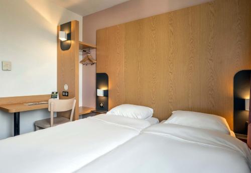 ein Schlafzimmer mit zwei weißen Betten und einem Schreibtisch in der Unterkunft B&B HOTEL Niort Marais Poitevin Est in Niort