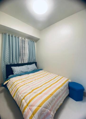 a bedroom with a bed with a striped comforter and a window at SHORE RESIDENCES 1 BD UNIT FOR RENT in Manila