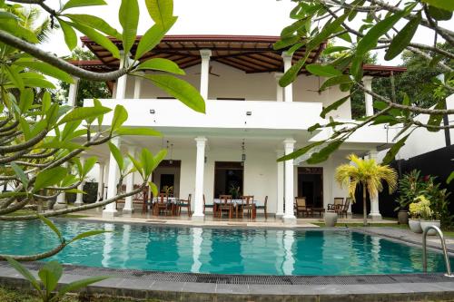 a pool in front of a house with tables and chairs at New Mangosteen Garden Villa in Hikkaduwa