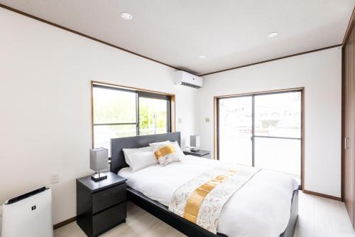 een slaapkamer met een groot bed met witte muren en ramen bij ヴィラかくれが in Sano