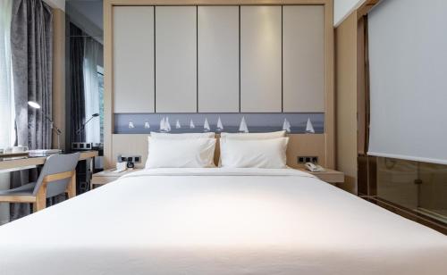 a bedroom with a large white bed and a desk at Atour Hotel Xiamen Xiagu Cruise Center in Xiamen