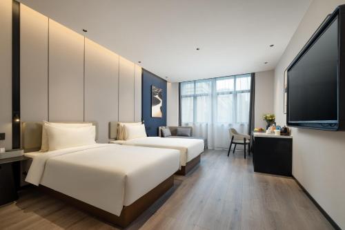 Atour Hotel Hangzhou Xintiandi Zhongda Intime في هانغتشو: سريرين في غرفة الفندق مع تلفزيون بشاشة مسطحة