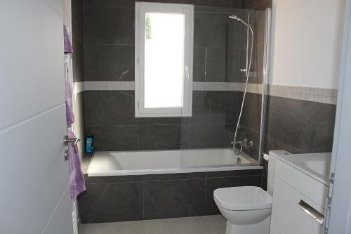 une salle de bain avec baignoire et toilettes et une fenêtre dans l'établissement Modern 4 bedroom villa, air-conditioning, swimming pool, private gardens, à Laroque-des-Albères