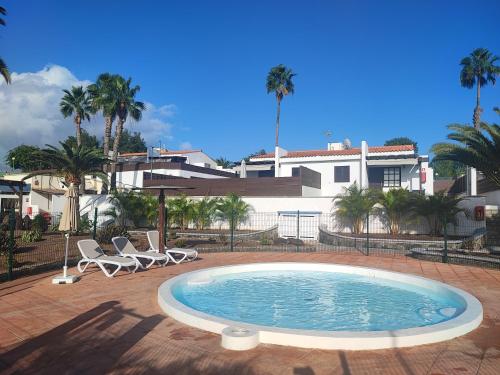 a swimming pool with two chairs and a house at Bungalow 1 Maspalomas Golf con piscina y jardín in San Bartolomé de Tirajana