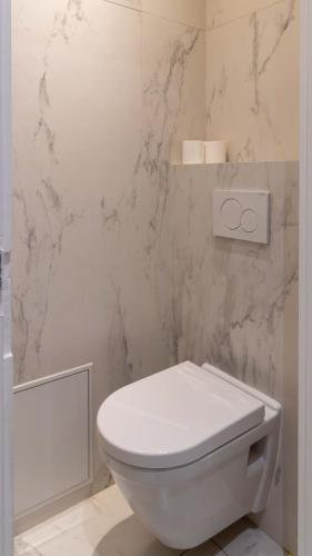 La salle de bains est pourvue de toilettes blanches et de murs en marbre. dans l'établissement Apartment Saint Germain des Près by Studio prestige, à Paris