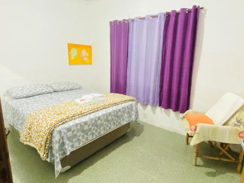 プライア・グランデにあるSeu Cantinho na Vila Tupi 3 Dormitóriosの紫色のカーテン、ベッド1台、椅子が備わるアパートメントです。